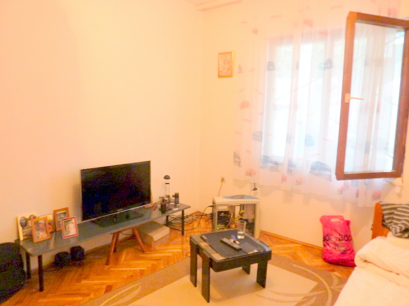 Living room in a house in Sutomore, Montenegro: bright room with parquet flooring, TV area, and a window with light curtains.