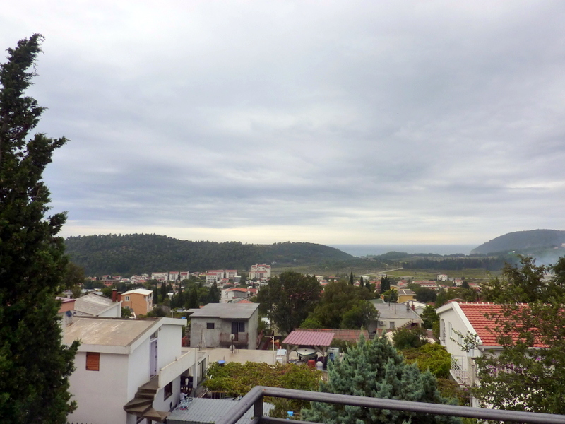 Panoramic view from a house balcony in Sutomore, Montenegro: green hills, low-rise buildings, and the sea horizon.