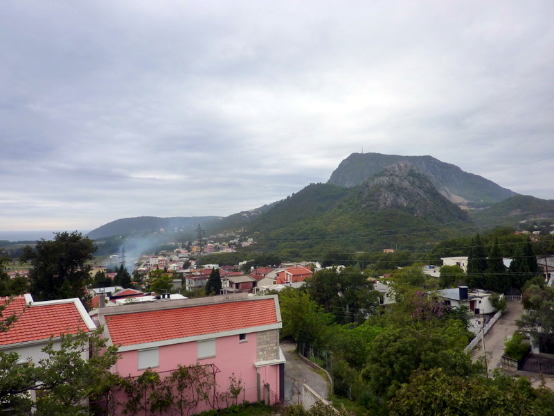 Panoramic view of the mountains and the town of Sutomore in Montenegro, private houses with red tiled roofs, and green landscape.