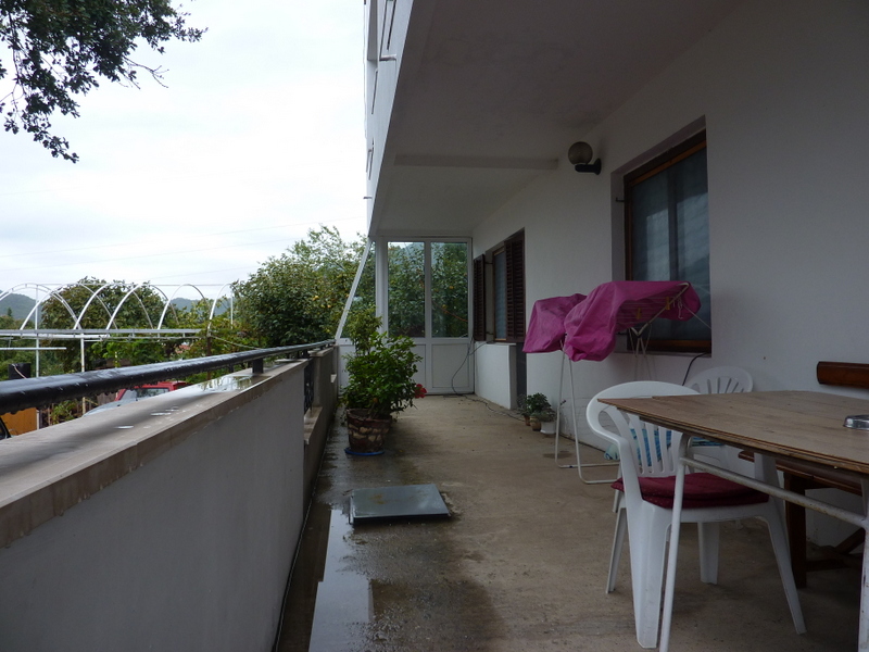 Spacious balcony of a house in Sutomore, Montenegro: wooden table, plastic chairs, and a view of the green garden.