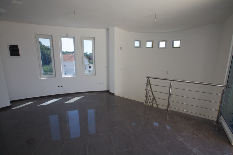 Bright living room in a house in Utjeha, Montenegro: gray tiled floor, white walls, panoramic windows, and a staircase with railings.