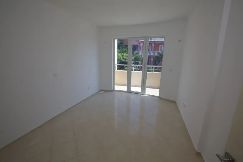 Empty room with beige tiles and sliding glass doors leading to a balcony.