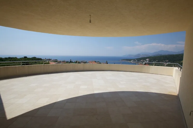 Wide tiled balcony with metal railing overlooking the sea and coastal landscape under a curved ceiling.