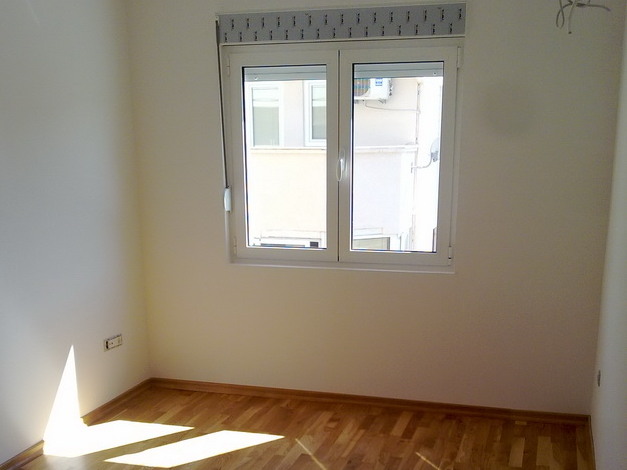Bright bedroom with parquet flooring and a plastic window in an apartment for sale in Budva, Montenegro.