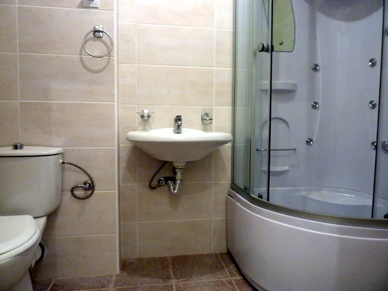 Bathroom featuring a toilet, wall-mounted sink, and corner shower unit on beige tiles.