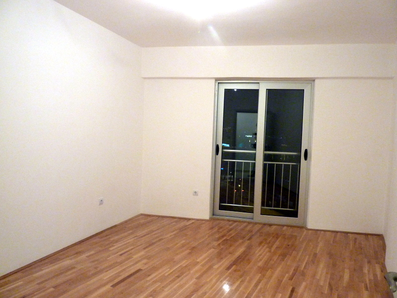 Bright living room with parquet flooring and access to the balcony in an apartment in Bečići, Montenegro. Empty room for renovation.