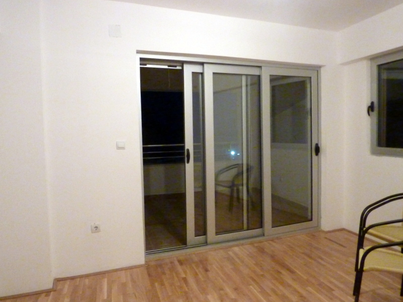 Living room in an apartment in Bečići, Montenegro: light finishes, panoramic sliding doors, and access to the balcony.