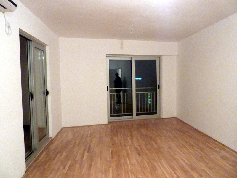 Bright living room with laminate flooring and panoramic windows in an apartment in Bečići, Montenegro. View of the balcony and the night city.