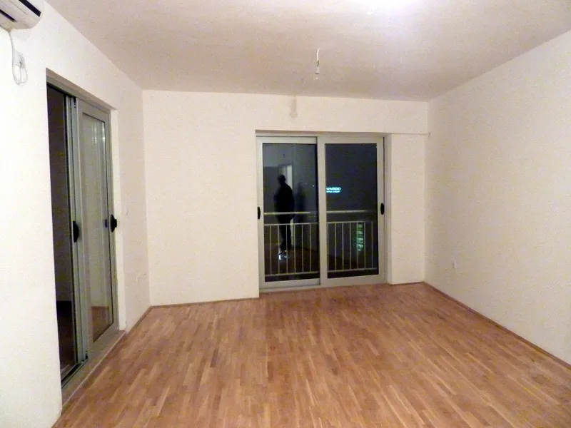 Empty room with laminate flooring, white walls, air conditioner, and sliding glass door to balcony.