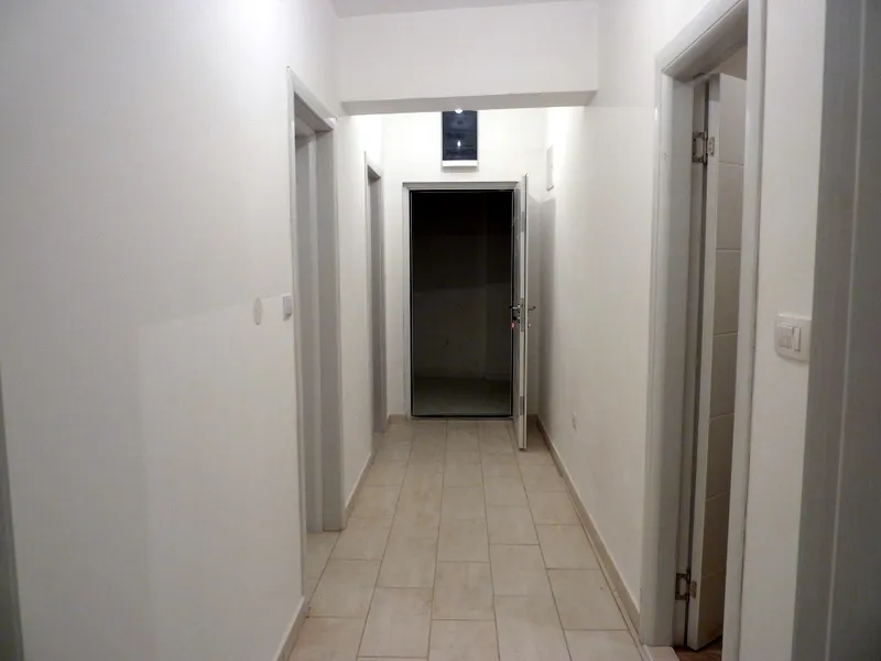 Long white hallway with tiled flooring and multiple doorways leading to adjacent rooms.
