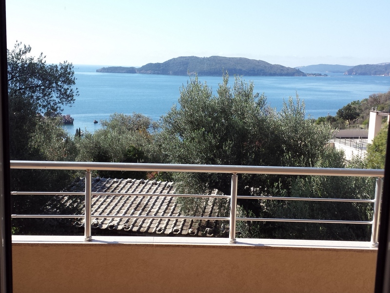 View from the apartment balcony in Pržno, Montenegro: panoramic view of the Adriatic Sea, St. Nicholas Island, and olive trees.