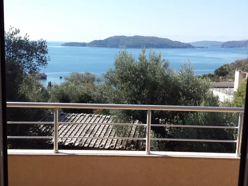 View from a balcony with metal railing overlooking the sea and islands.