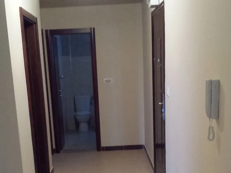 Hallway with dark wood doors and a visible toilet at the end. A wall-mounted phone is on the right.