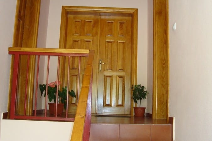 Hotel interior in Čanj, Montenegro: wooden double doors, a staircase with red railings, and houseplants.