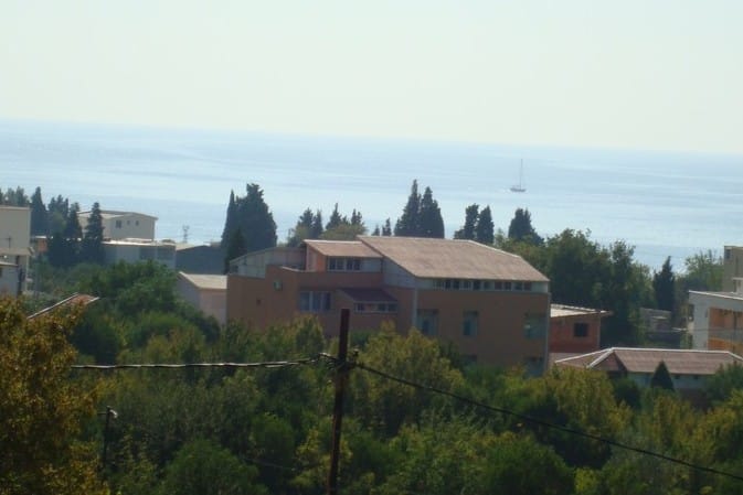 View of a hotel in Čanj, Montenegro: a building surrounded by greenery with panoramic views of the Adriatic Sea and a yacht.