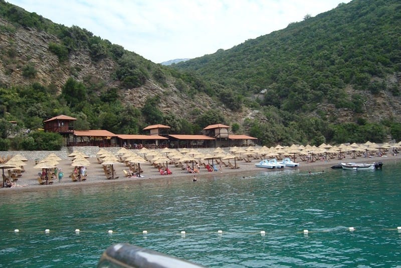 Sea view of the hotel’s private beach in Čanj, Montenegro: sun loungers, thatched umbrellas, and a mountainous coastal landscape.