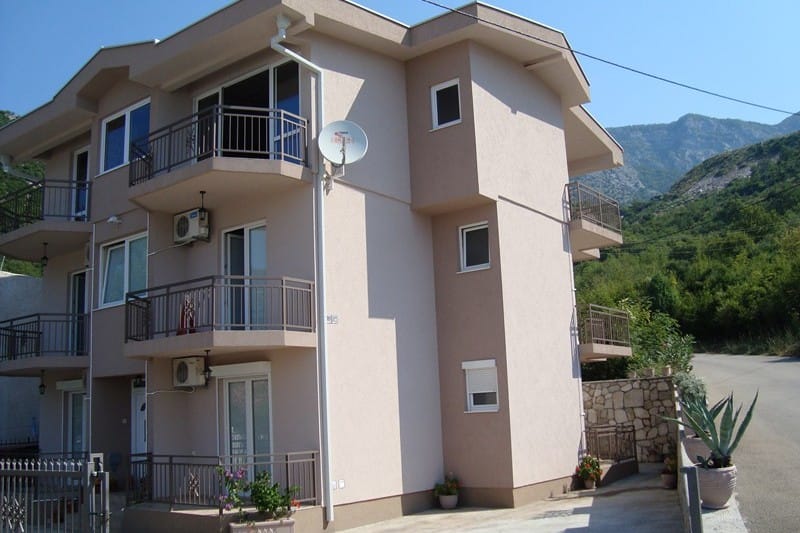 Three-story hotel in Čanj, Montenegro: building facade with balconies, air conditioners, and mountain views.