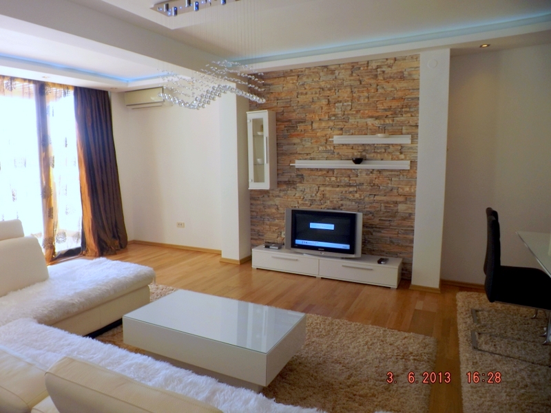 Living room in an apartment in Pržno, Montenegro: light-colored furniture, a wall finished with decorative stone, and a panoramic window.