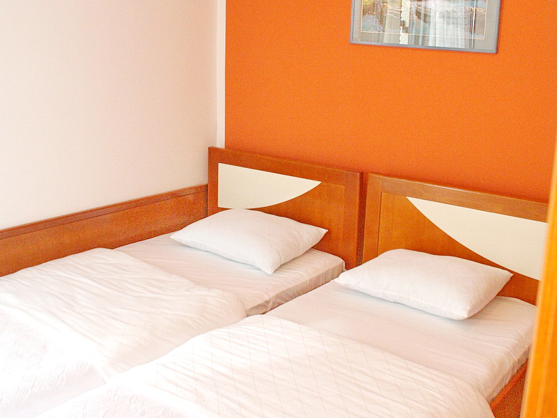 Bedroom with two single beds in a hotel in Tivat, Montenegro: wooden furniture and an orange wall.