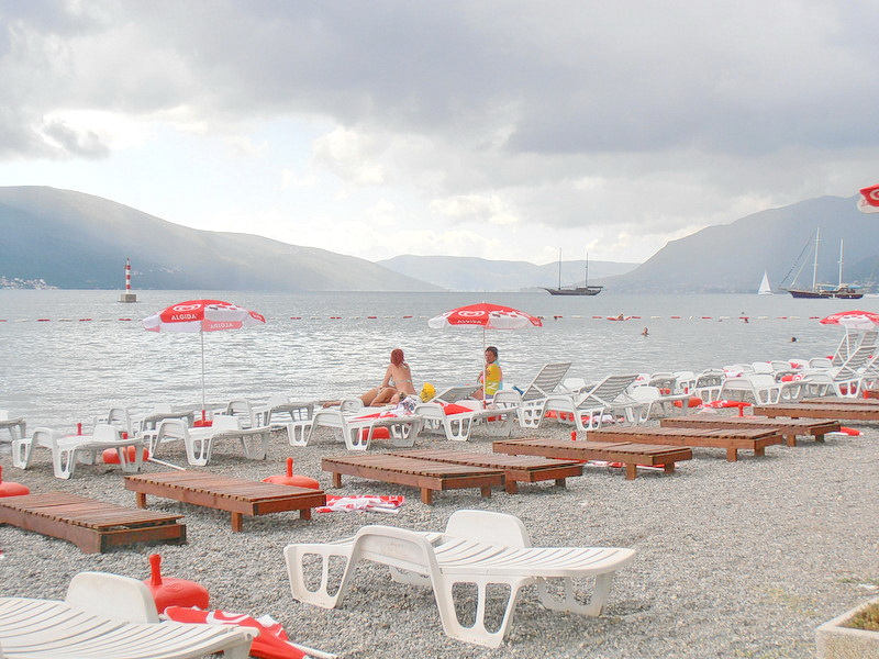 Beach with sun loungers and umbrellas by the sea in Tivat, Montenegro: view of the bay, mountains, and yachts near the hotel.