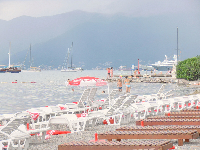 Hotel beach in Tivat, Montenegro: white sun loungers by the sea, views of yachts, the bay, and mountains in the resort area.