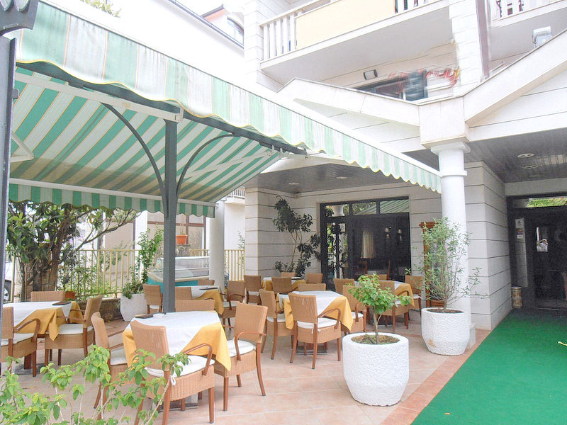Cozy summer terrace of the hotel restaurant in Tivat, Montenegro, with tables, wicker chairs, and a green canopy.