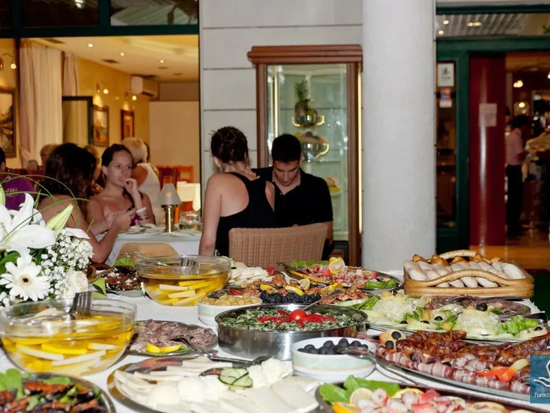 Dining hall featuring a lavish buffet spread with various dishes, flowers, and seated guests in the background.