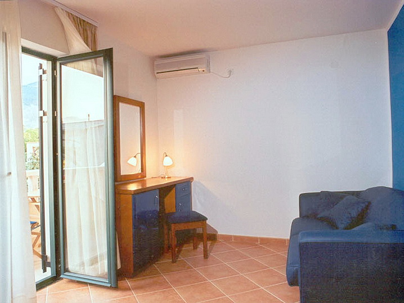 Living room interior in a hotel in Tivat, Montenegro: blue sofa, vanity table with mirror, and access to the balcony.