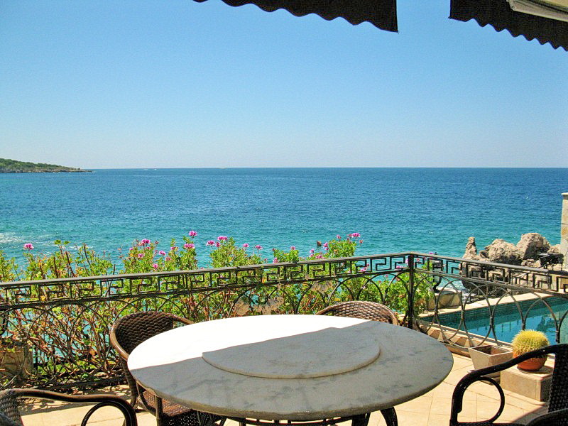 Villa terrace in Dobra Voda, Montenegro: sea view, wicker chairs, marble table, and a pool by the railing.