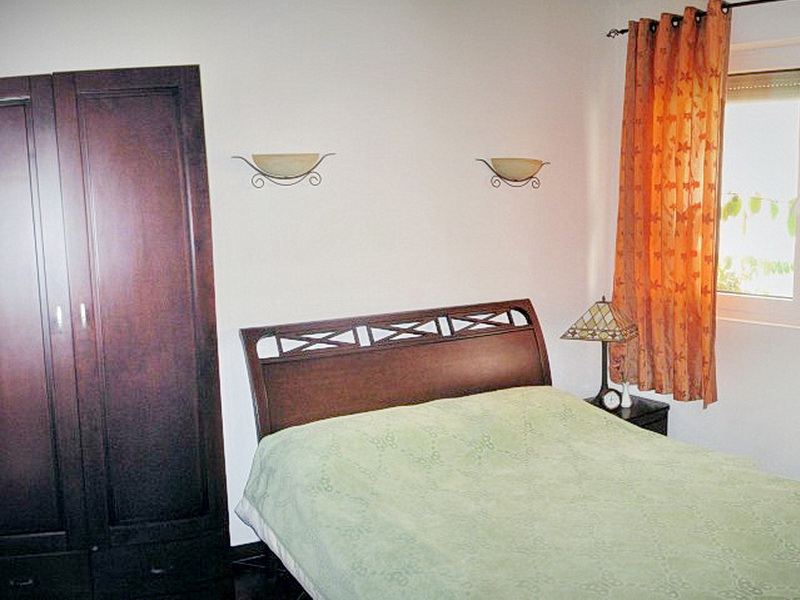 Bedroom with a double bed, dark wardrobe, and orange curtains in a villa in Dobra Voda, Montenegro.