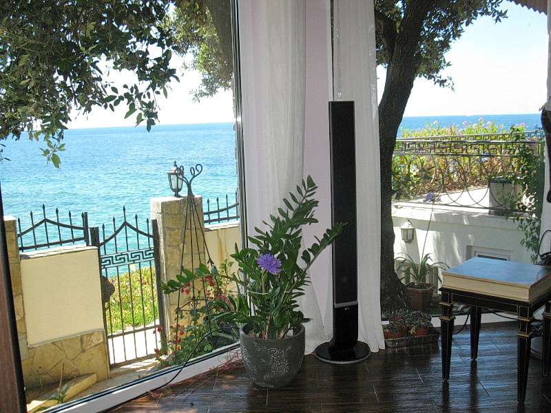 View from the villa living room in Dobra Voda, Montenegro: panoramic windows, a terrace with a wrought-iron fence, and a direct sea view.