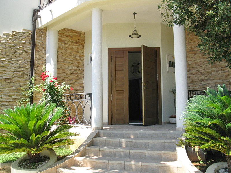 Entrance to a villa in Dobra Voda, Montenegro: stone facade, white columns, staircase, and palm trees by the porch.