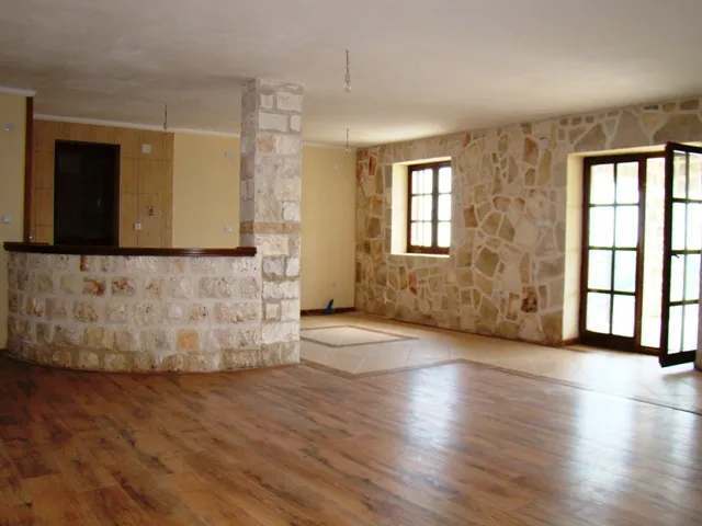 Spacious room with wood flooring, stone wall, and a curved stone bar counter leading to the kitchen area.
