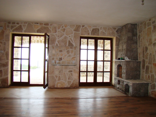 Living room with stone wall finishes and a fireplace in a house in Petrovac, Montenegro, with access to the terrace through panoramic doors