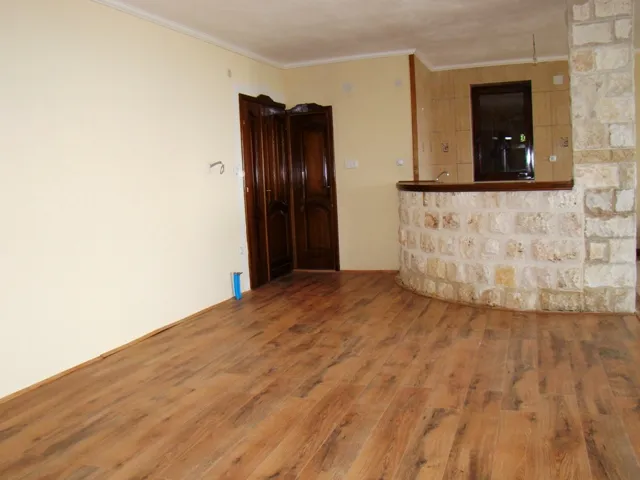 Empty room with laminate flooring and a stone bar counter leading to the kitchen area.