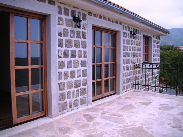 Stone terrace of a house in Petrovac, Montenegro, with panoramic wooden doors and mountain views.