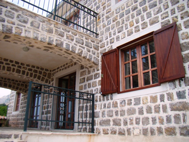 House facade of natural stone with wooden shutters and a wrought-iron balcony in Petrovac, Montenegro.