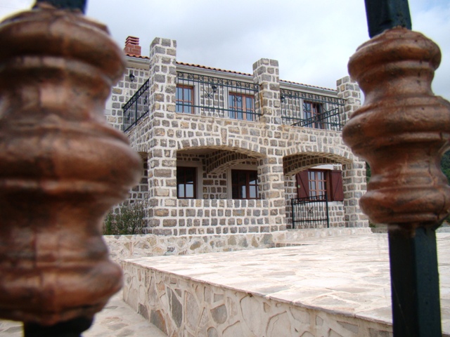 Two-story natural stone house with a terrace and wrought-iron railings in Petrovac, Montenegro.