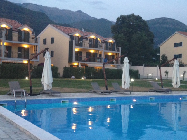 Outdoor pool with sun loungers at a residential complex in Budva, Montenegro, with mountains in the background at dusk.