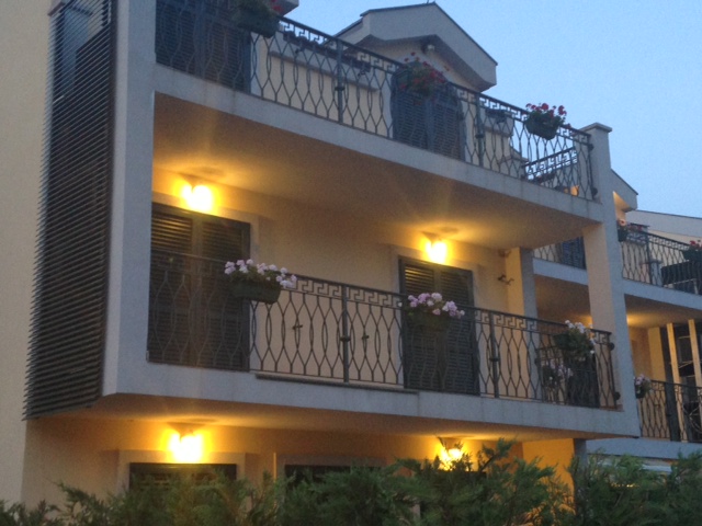 Facade of a residential building in Budva, Montenegro: cozy balconies with wrought-iron railings, flowers, and evening lighting.