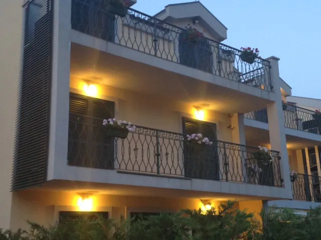 View of building facade with balconies adorned with flower boxes and wrought iron railings under evening lighting.