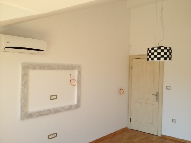 Bright living room in an apartment in Budva, Montenegro: air conditioner, TV niche, light-colored door, and a stylish light fixture.