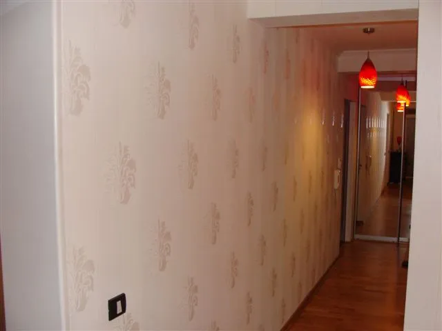 Hallway with patterned wallpaper, wooden floor, and red pendant lights visible further down the corridor.