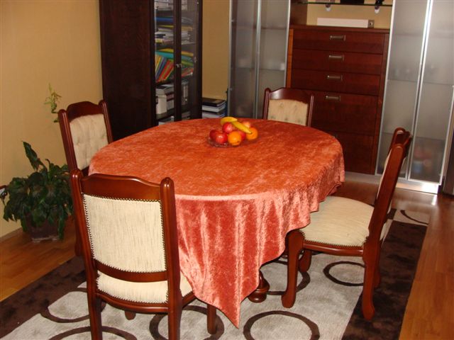 Dining area in the apartment living room in Budva, Montenegro: a round table with an orange tablecloth and wooden chairs.