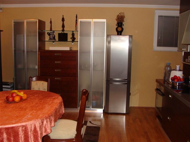 Kitchen interior in an apartment in Budva, Montenegro: dining table, wooden furniture, refrigerator, and kitchen cabinets.