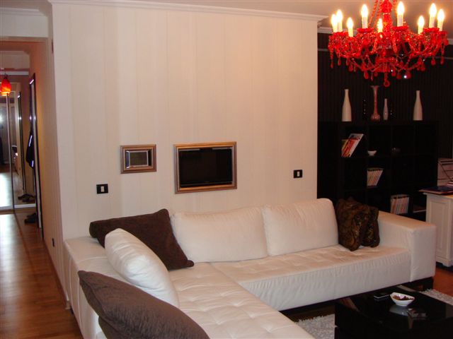 Living room in an apartment in Budva, Montenegro: white corner sofa, red chandelier, and built-in TV in the interior.