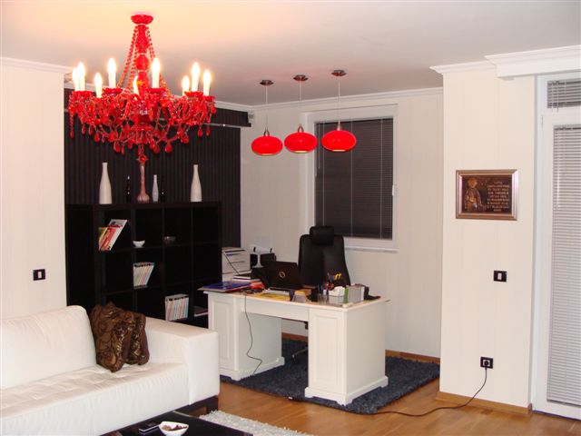 Modern living room with a workspace in an apartment in Budva, Montenegro: white furniture, a red chandelier, and parquet flooring.