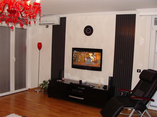 Living room in an apartment in Budva, Montenegro: modern interior with a red chandelier, TV area, and black furniture.