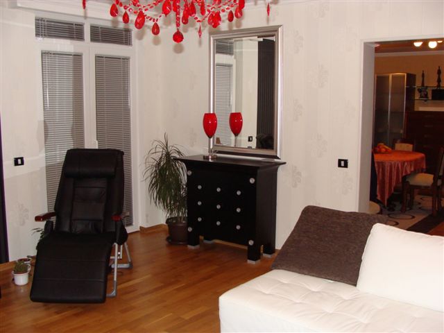 Living room in an apartment in Budva, Montenegro: bright interior, black furniture, mirror, and a red chandelier, parquet floor.