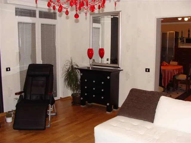 Living room with black recliner, white sofa, red chandelier, mirror above black chest of drawers.